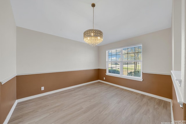 unfurnished room with a chandelier, baseboards, and wood finished floors