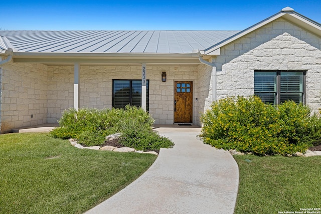 doorway to property featuring metal roof, a standing seam roof, stone siding, and a lawn