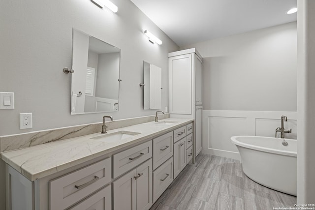 full bath with double vanity, a wainscoted wall, a freestanding bath, and a sink