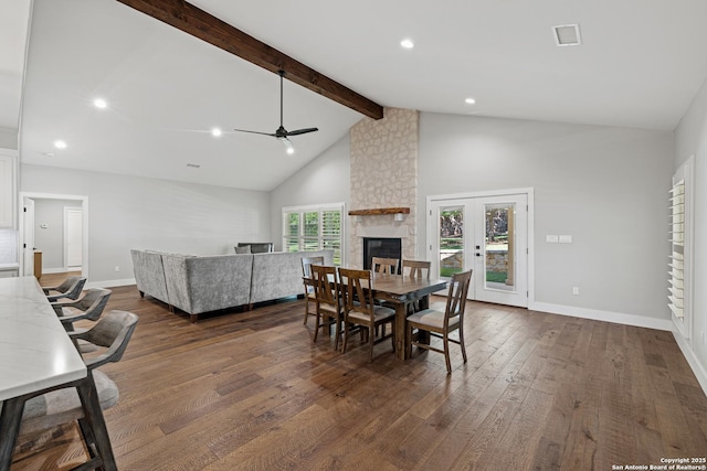 dining room with baseboards, visible vents, dark wood-type flooring, beamed ceiling, and a stone fireplace