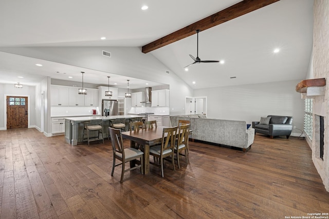 dining area with high vaulted ceiling, a stone fireplace, dark wood-style flooring, visible vents, and beamed ceiling