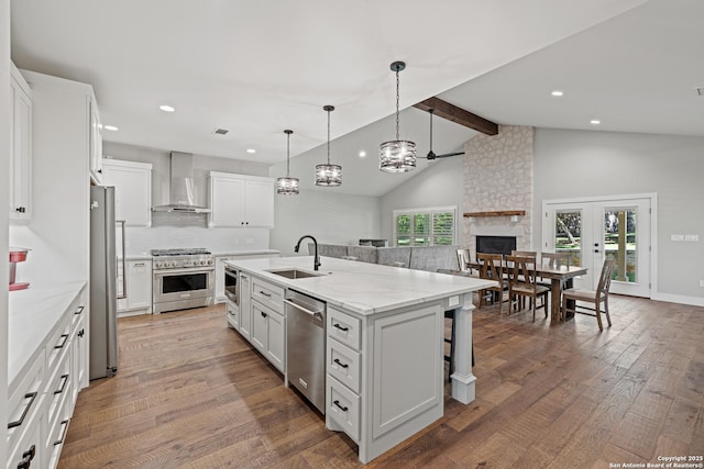 kitchen featuring beam ceiling, appliances with stainless steel finishes, a sink, wall chimney range hood, and hardwood / wood-style floors