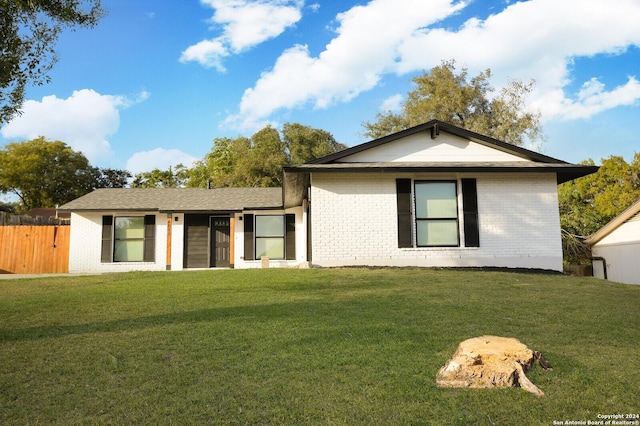 rear view of house featuring brick siding, a lawn, and fence