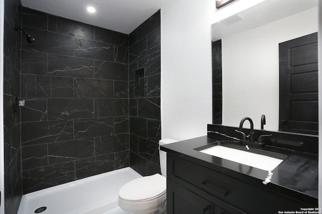 bathroom with visible vents, vanity, a tile shower, and toilet