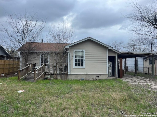 back of house featuring dirt driveway, a lawn, an attached carport, crawl space, and fence