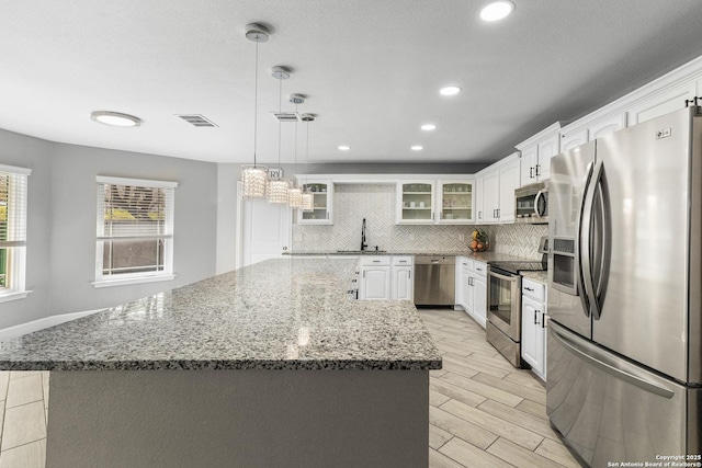 kitchen featuring wood finish floors, a kitchen island, visible vents, appliances with stainless steel finishes, and backsplash