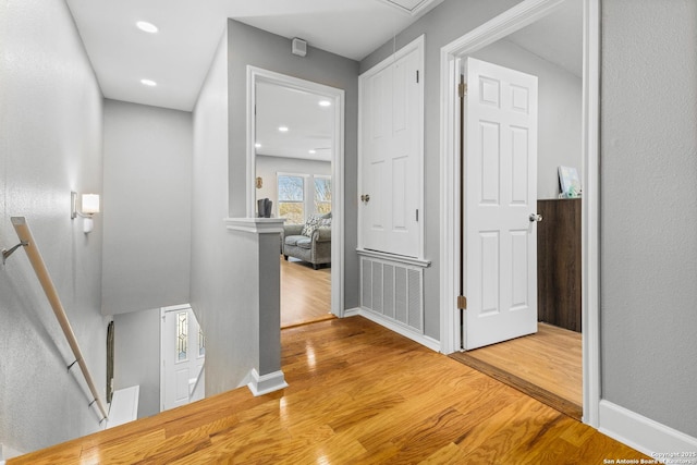 hallway with attic access, baseboards, visible vents, wood finished floors, and an upstairs landing