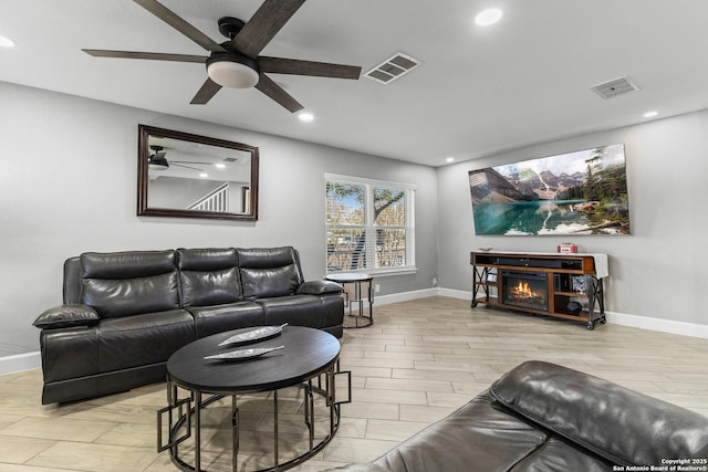 living room with a warm lit fireplace, baseboards, visible vents, and wood finished floors