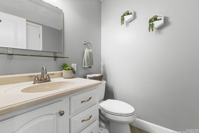 bathroom featuring toilet, a textured wall, and vanity