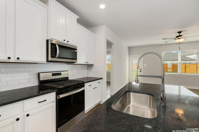 kitchen featuring tasteful backsplash, white cabinets, dark stone counters, stainless steel appliances, and a sink