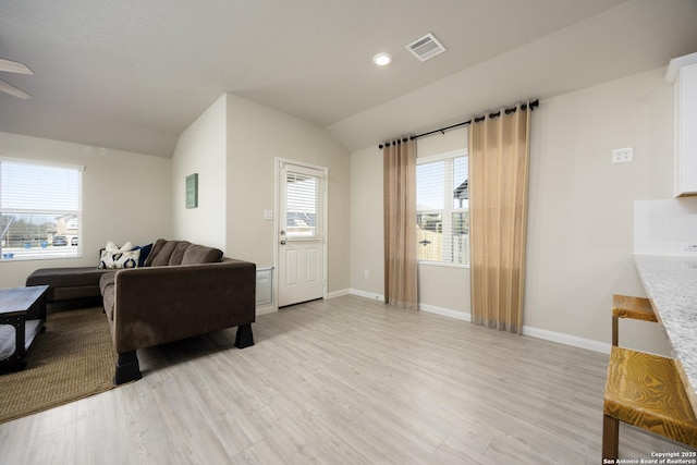 living area featuring vaulted ceiling, light wood-style flooring, visible vents, and baseboards