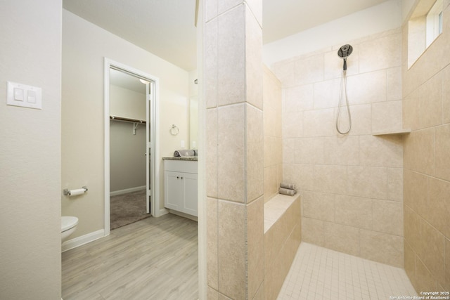 bathroom featuring baseboards, toilet, wood finished floors, vanity, and a walk in shower