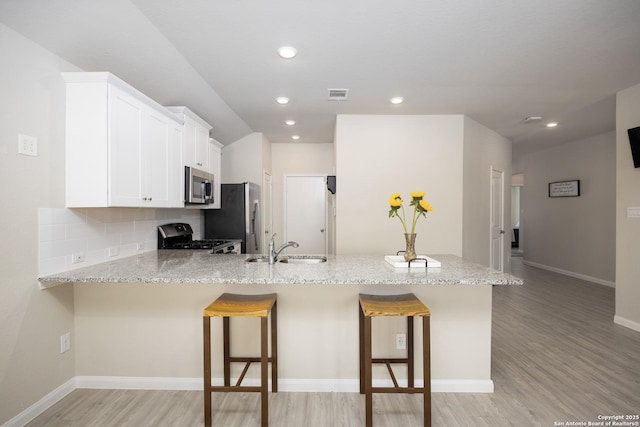 kitchen featuring a breakfast bar, appliances with stainless steel finishes, a sink, light stone countertops, and a peninsula