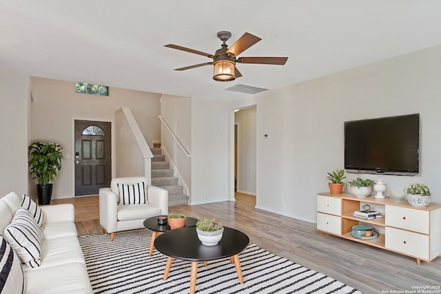 living area with ceiling fan, wood finished floors, visible vents, baseboards, and stairway