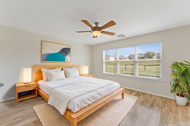 bedroom featuring a ceiling fan, light wood-style flooring, visible vents, and baseboards