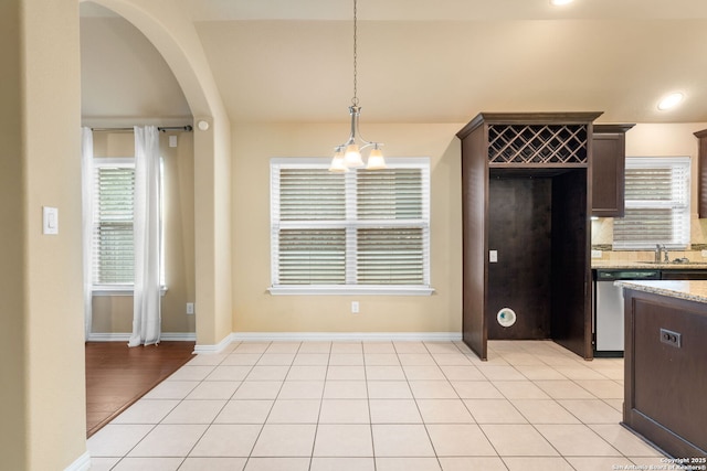 kitchen with lofted ceiling, stainless steel dishwasher, light tile patterned flooring, dark brown cabinetry, and a sink