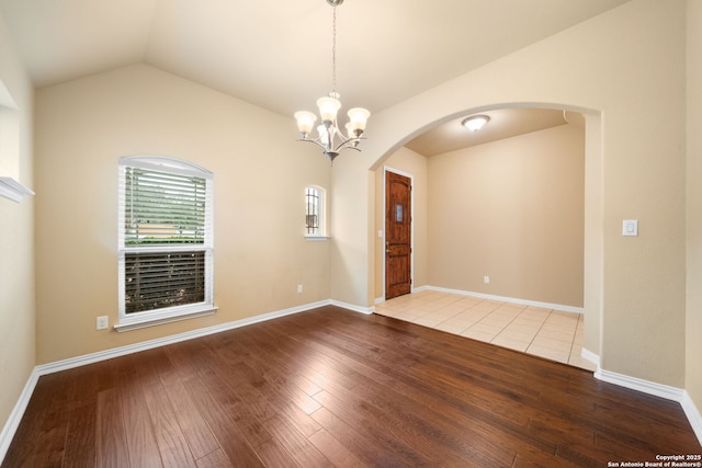 empty room with baseboards, arched walkways, lofted ceiling, wood finished floors, and a notable chandelier