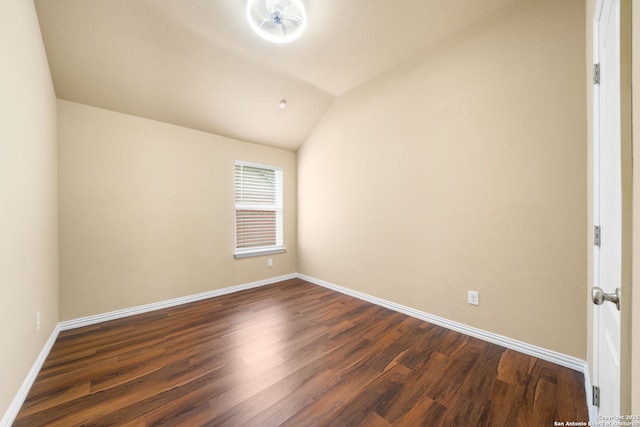 empty room featuring lofted ceiling, dark wood-type flooring, and baseboards