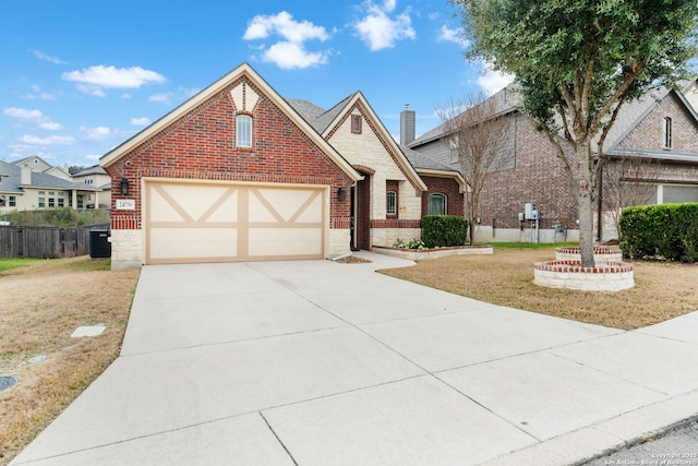 tudor-style house with concrete driveway, brick siding, fence, and an attached garage