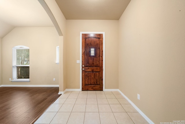 foyer with light tile patterned floors, baseboards, arched walkways, and vaulted ceiling