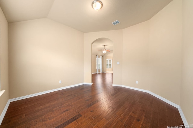 empty room featuring visible vents, arched walkways, baseboards, dark wood-style floors, and vaulted ceiling