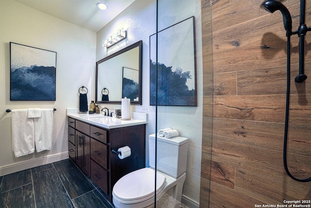 full bath with toilet, a tile shower, vanity, and baseboards