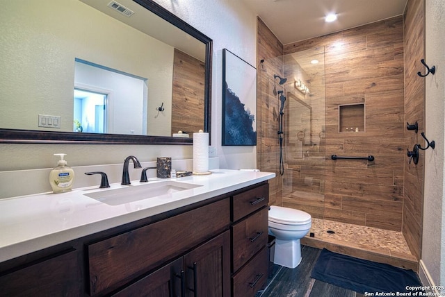 full bathroom with visible vents, toilet, a tile shower, vanity, and wood finished floors