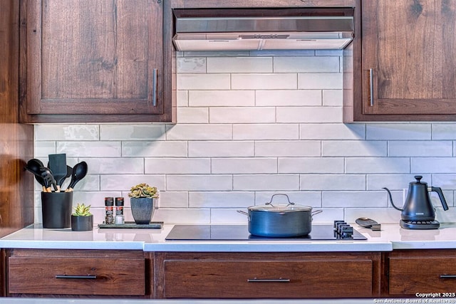 kitchen featuring black electric stovetop, exhaust hood, light countertops, dark brown cabinets, and decorative backsplash