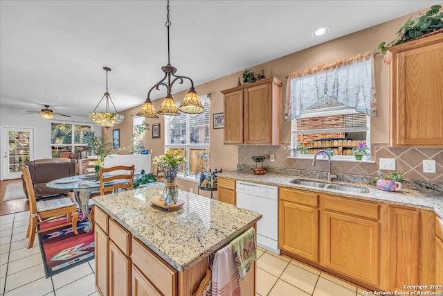 kitchen with a center island, tasteful backsplash, a sink, light stone countertops, and dishwasher