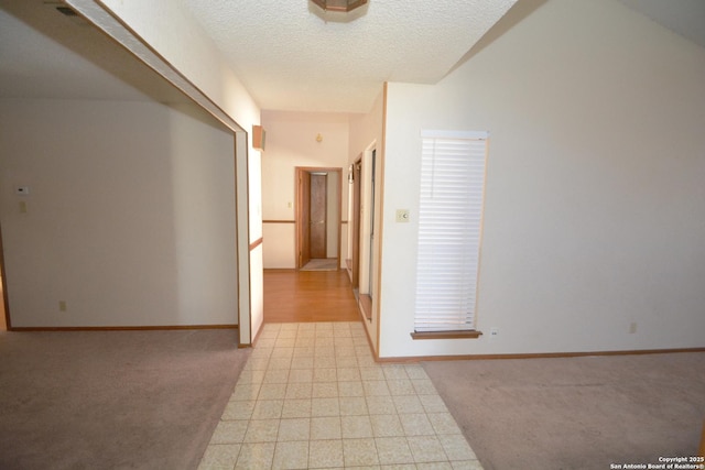 corridor with a textured ceiling, light carpet, and baseboards