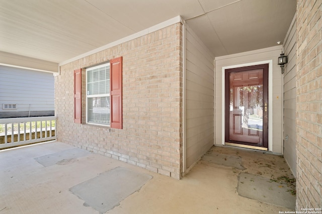 entrance to property featuring a porch and brick siding