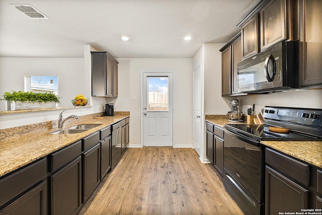 kitchen featuring light wood finished floors, visible vents, light stone counters, black appliances, and a sink