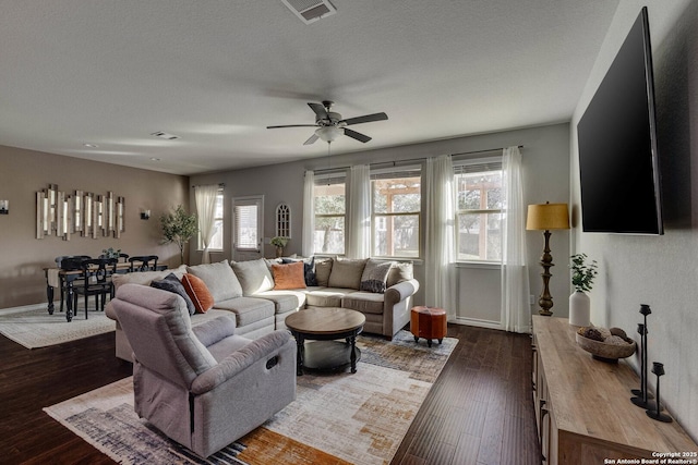 living area featuring baseboards, dark wood-type flooring, visible vents, and a ceiling fan