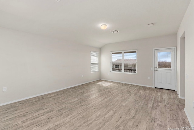 spare room featuring light wood-type flooring, baseboards, visible vents, and vaulted ceiling