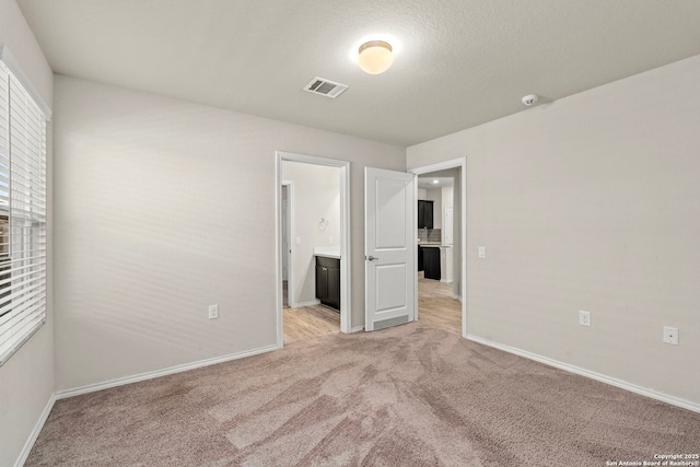 unfurnished bedroom featuring light carpet, baseboards, visible vents, and connected bathroom