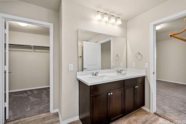 full bathroom with double vanity, a spacious closet, a sink, and wood finished floors