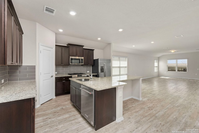 kitchen with stainless steel appliances, visible vents, light wood-style floors, open floor plan, and an island with sink