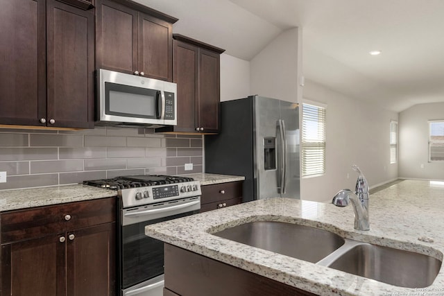 kitchen with lofted ceiling, stainless steel appliances, a sink, dark brown cabinets, and decorative backsplash