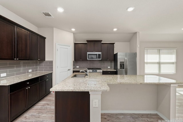 kitchen with a kitchen island with sink, stainless steel appliances, a sink, visible vents, and light wood finished floors