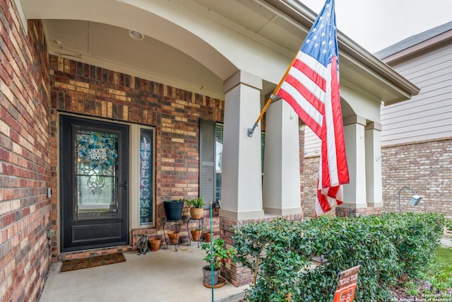 entrance to property featuring a porch and brick siding