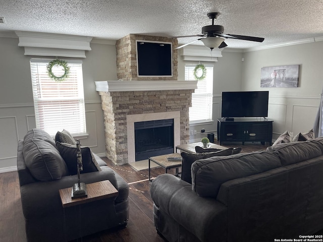 living area with dark wood-style floors, crown molding, a decorative wall, a stone fireplace, and a textured ceiling