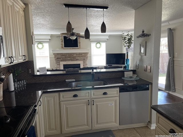 kitchen with cream cabinets, a sink, open floor plan, dishwasher, and dark countertops