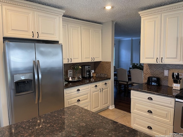 kitchen with dark stone countertops, a textured ceiling, stainless steel fridge with ice dispenser, and light tile patterned floors