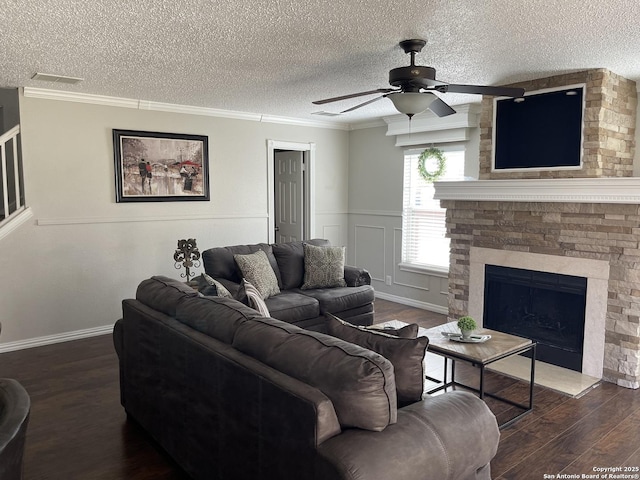 living room featuring a ceiling fan, dark wood-type flooring, a textured ceiling, crown molding, and a fireplace