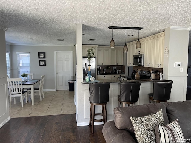 kitchen featuring cream cabinetry, crown molding, stainless steel appliances, dark countertops, and open floor plan