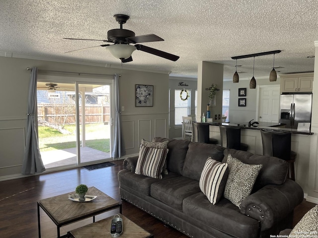 living area with a wainscoted wall, a decorative wall, dark wood-style flooring, and crown molding