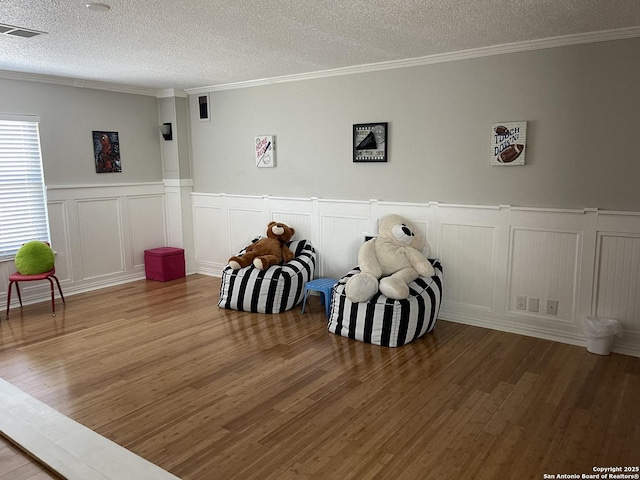 game room featuring a textured ceiling, wood finished floors, visible vents, and crown molding