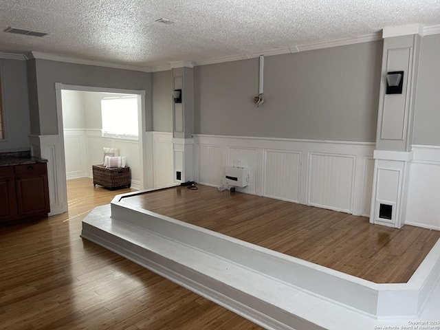 interior space featuring visible vents, a wainscoted wall, ornamental molding, wood finished floors, and a textured ceiling