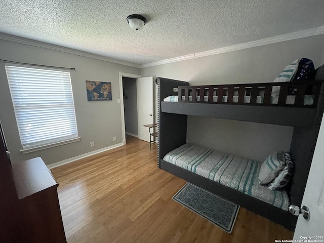 bedroom with crown molding, a textured ceiling, baseboards, and wood finished floors