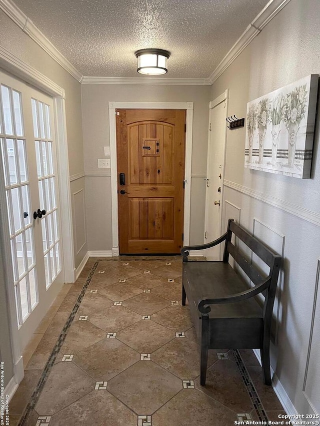 foyer featuring a textured ceiling, ornamental molding, wainscoting, and a decorative wall